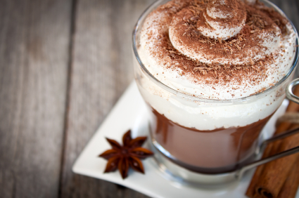 A glass of hot chocolate with whipped cream and chocolate shavings, on a napkin.