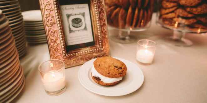 Ice cream cookie sandwich plated on a table, with two lit candles and a gold picture frame.