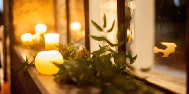 Lit candles on a windowsill, with small leafy plants.