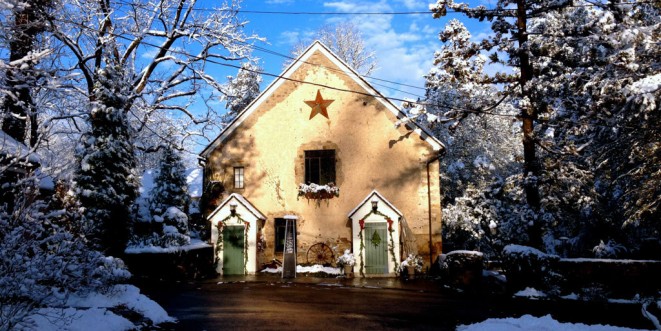 Beige stone building with a red star and two green doors, landscape covered in snow.