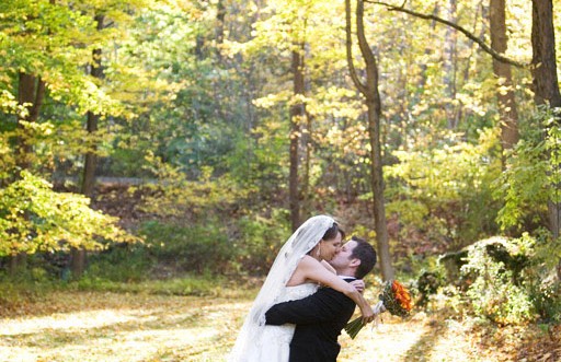 Bride and groom hugging and kissing, with green woodsy trees in the background.