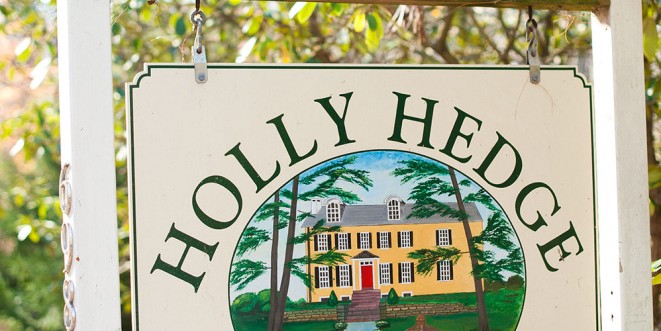 Close-up of HollyHedge Estate white hanging sign that reads "Holly Hedge" and has a graphic of the estate