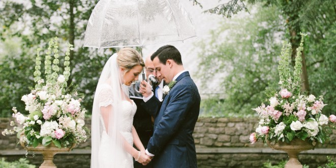 A bride and groom holding hands at the altar, with the officiant holding an umbrella over them.