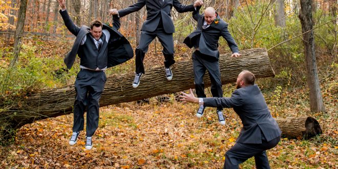 Groomsmen in the woods jumping off of a log together.