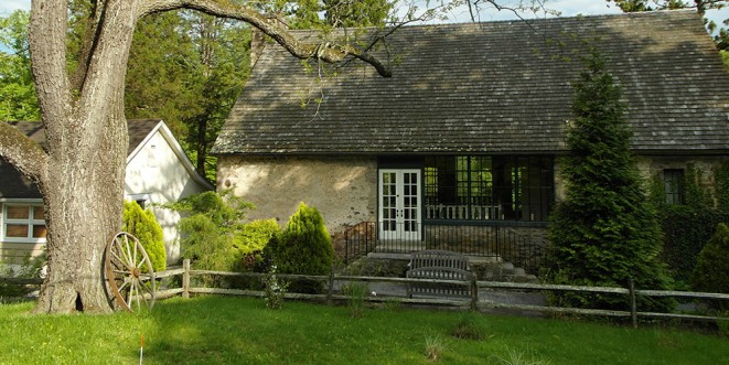 An older, stone building situated behind a field of grass with a large tree trunk.