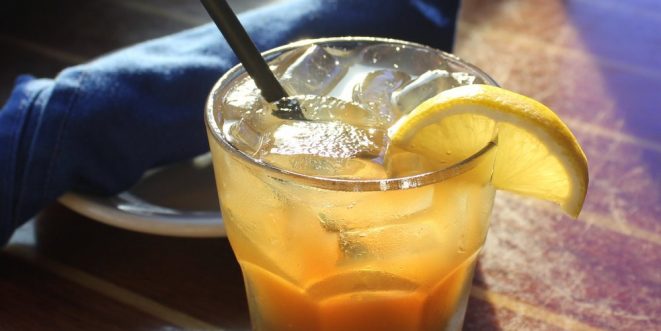 An orange drink in a glass, with ice and a lemon wedge.