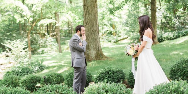 A first-look between bride and groom, standing in a luscious green, wooded area.