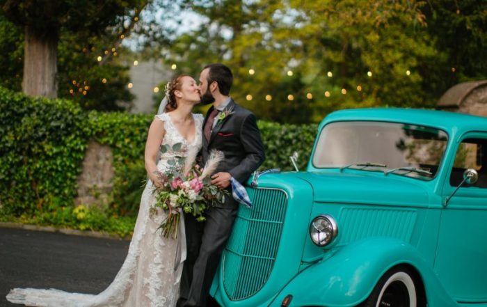 Bride and groom in front of an antique turquoise truck, kissing and holding a bouquet.