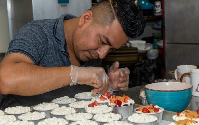 A chef in kitchen, carefully placing fruit on top of dessert cups.