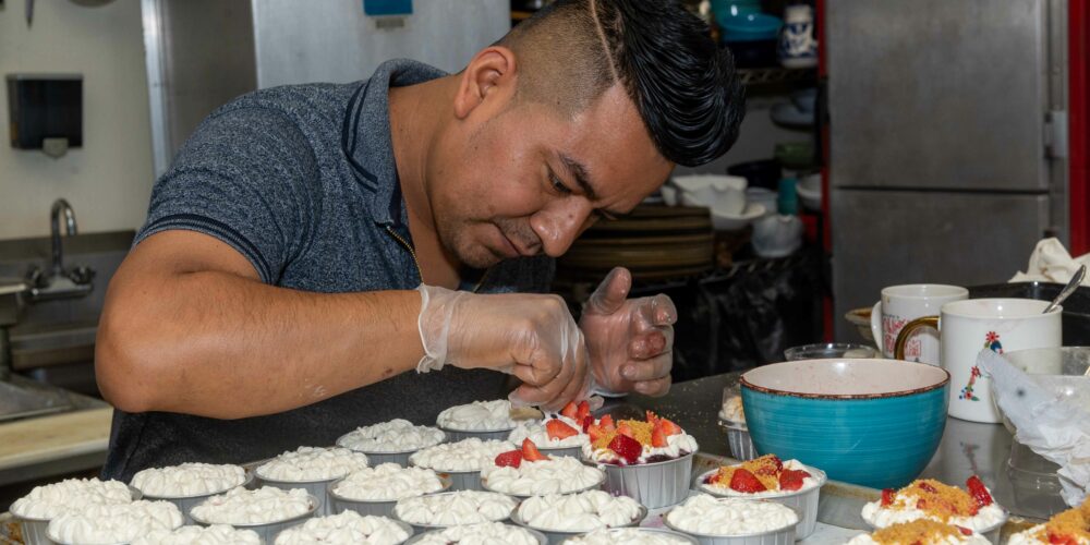 A chef in kitchen, carefully placing fruit on top of dessert cups.