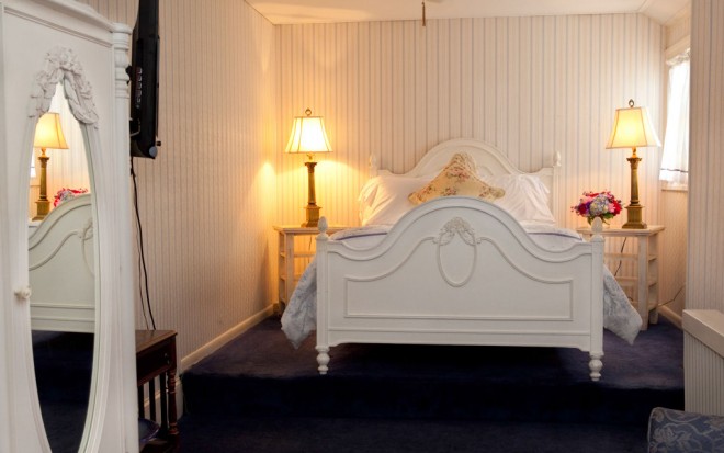 Photo of Room 1: A standard room with a bed with white frame, two lamps, and dark carpet