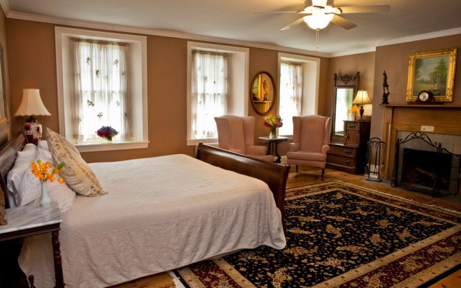 Photo of Room 10: The master suite has a king size dark wood bed, a fireplace, wingback chairs, large windows, and wood flooring