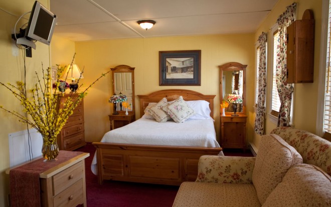 Photo of Room 6: A bright standard room with a light wood bed, nightstands, dresser, small couch, and TV on the wall